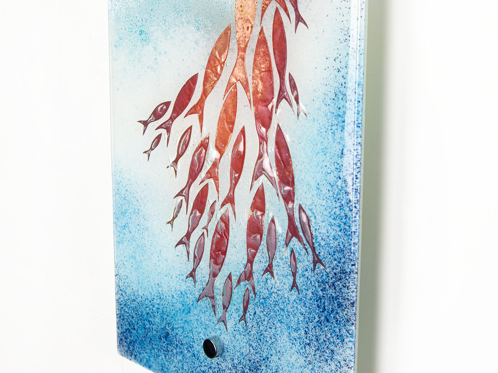 Close up of fused glass wall panel in an ocean inspired design with copper fish and soft ocean colours. 