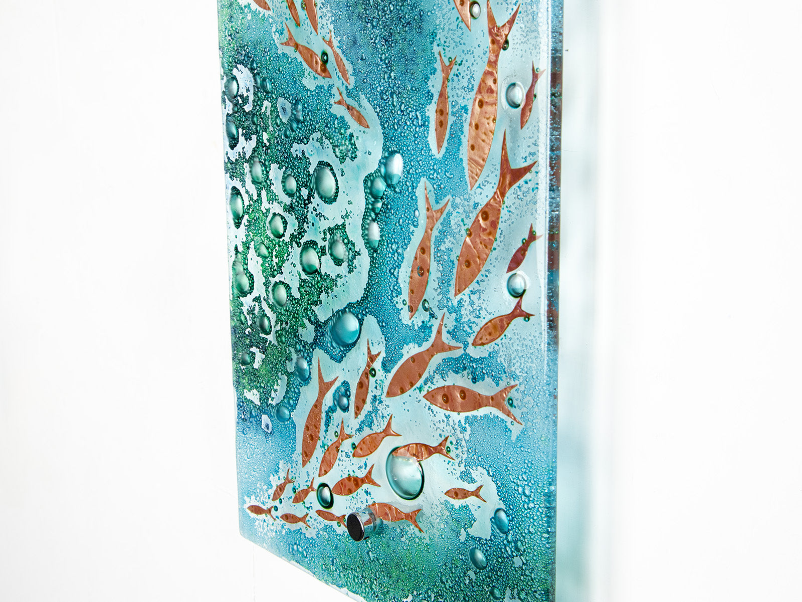 Details of organic texture on fused glass wall panel with coastal green colours and copper fish. A wall art piece inspired by the ocean.