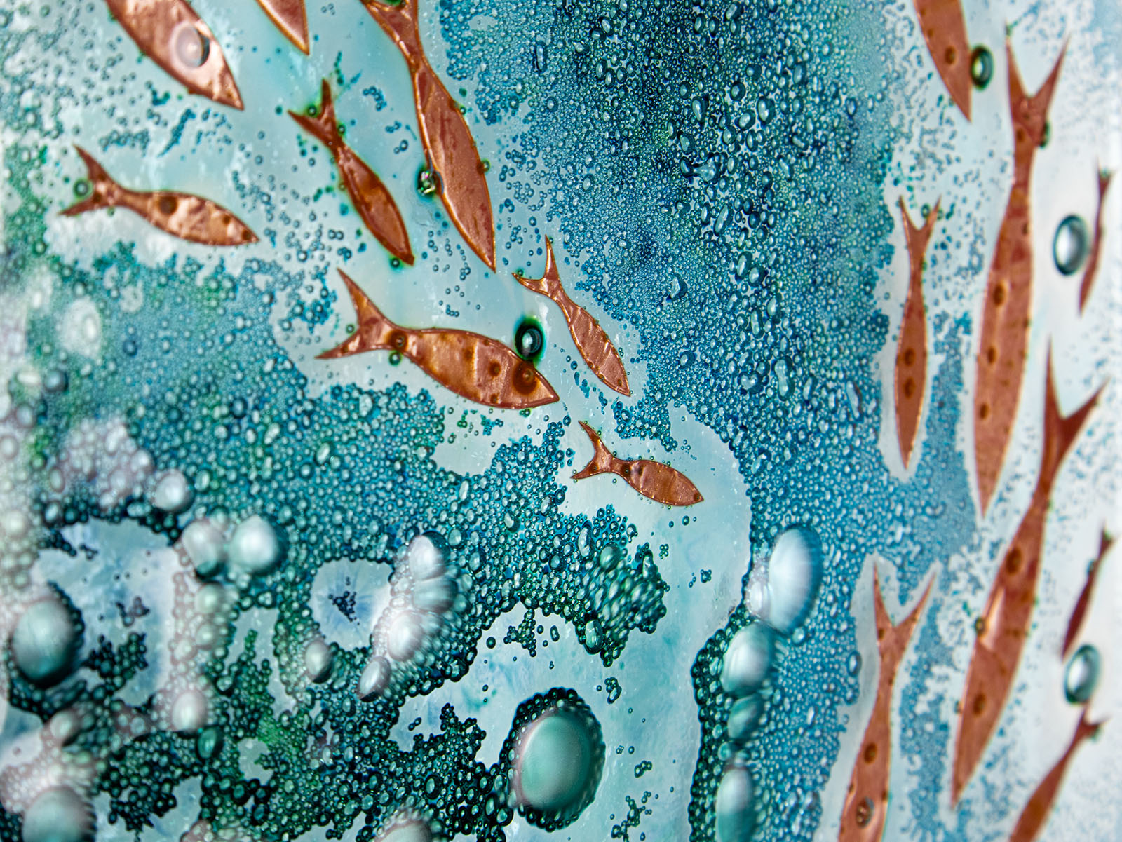 Close up of fused glass wall panel with coastal green colours and copper fish. A wall art piece inspired by the ocean.