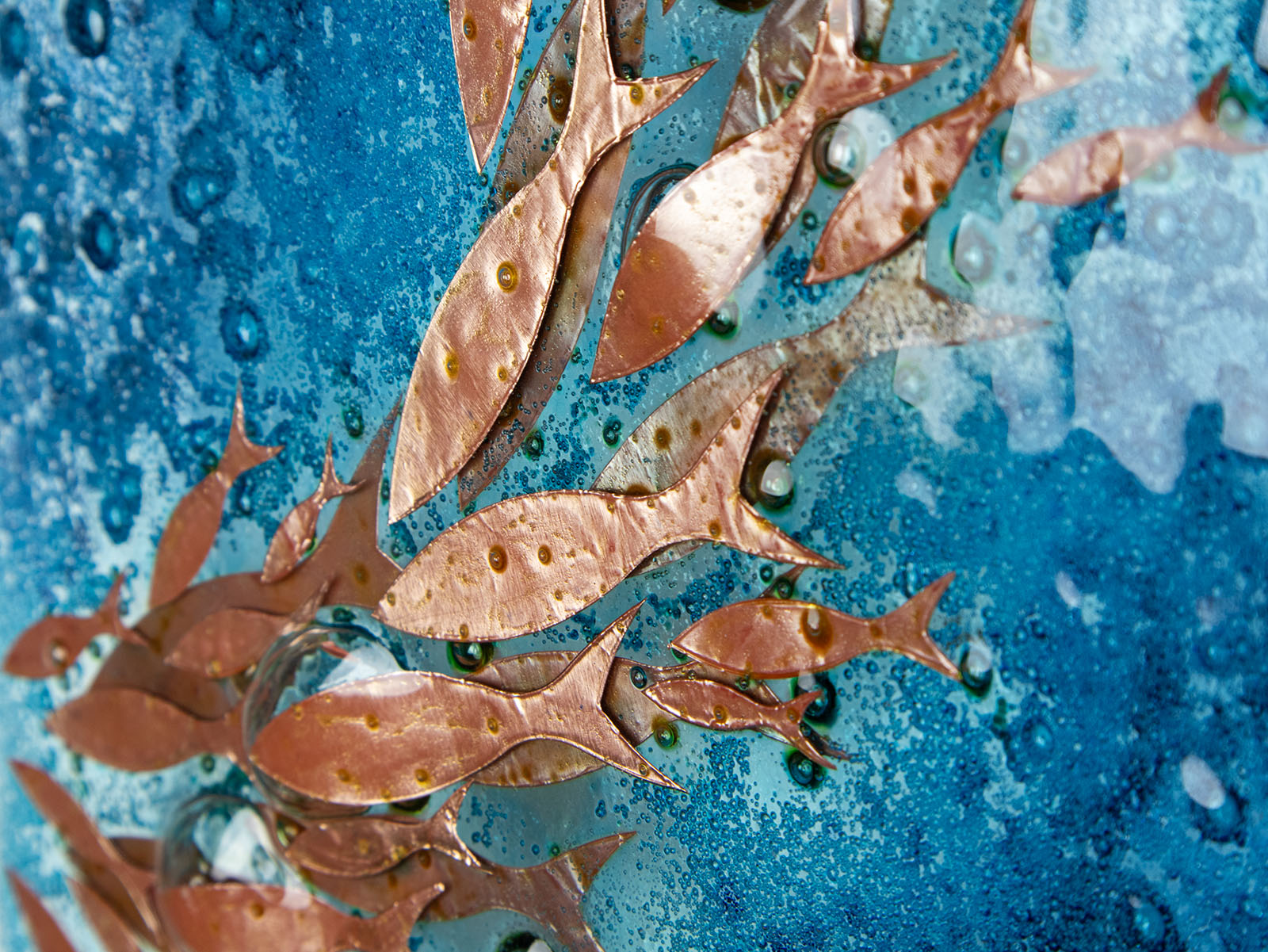 Details of copper fish on a fused glass wall panel with bubbled blue colours. An organic and ocean inspired piece of wall art. 