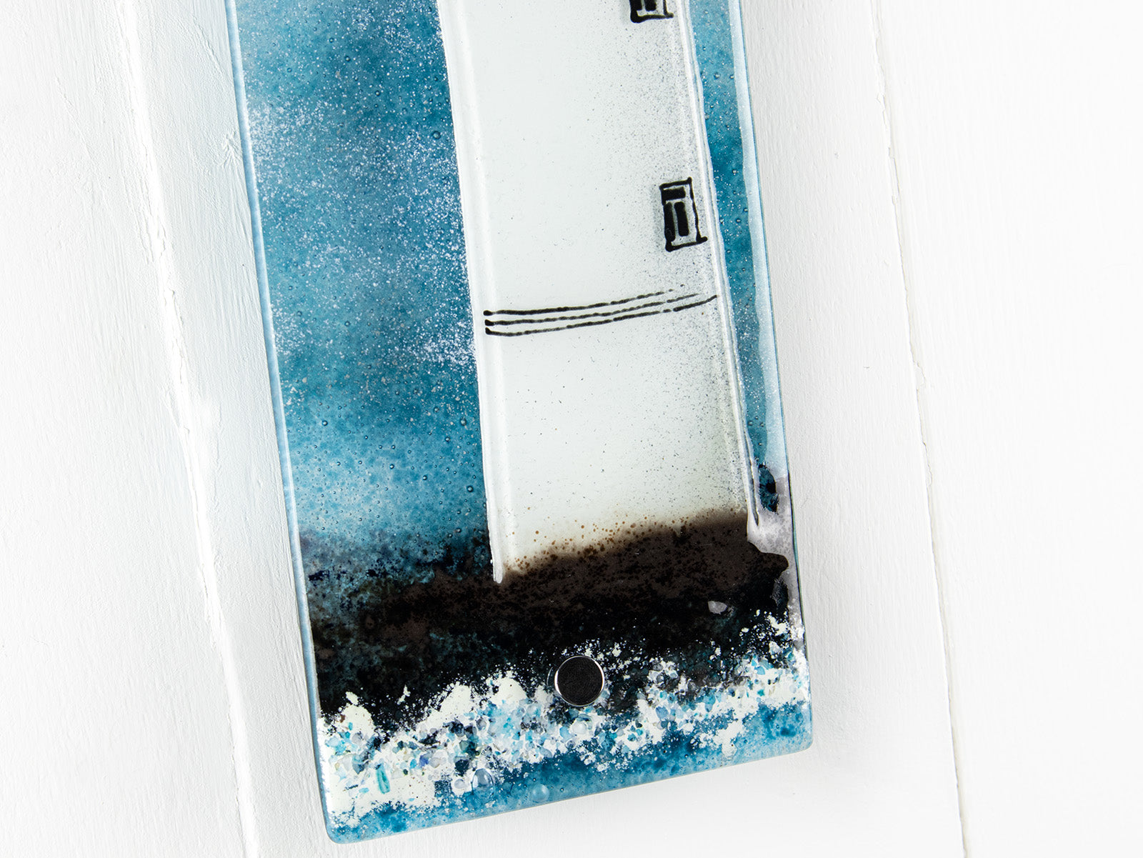 Textural detailing of small fused glass wall panel, featuring a lighthouse design in a teal blue colour-way. 
