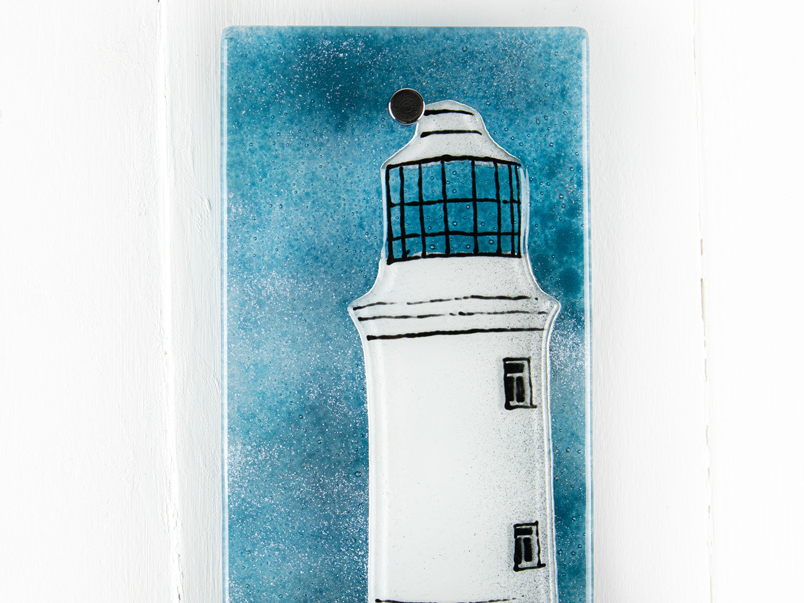 Close up of small fused glass wall panel, featuring a lighthouse design in a teal blue colour-way. 