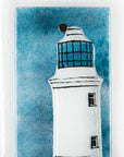 Close up of small fused glass wall panel, featuring a lighthouse design in a teal blue colour-way. 