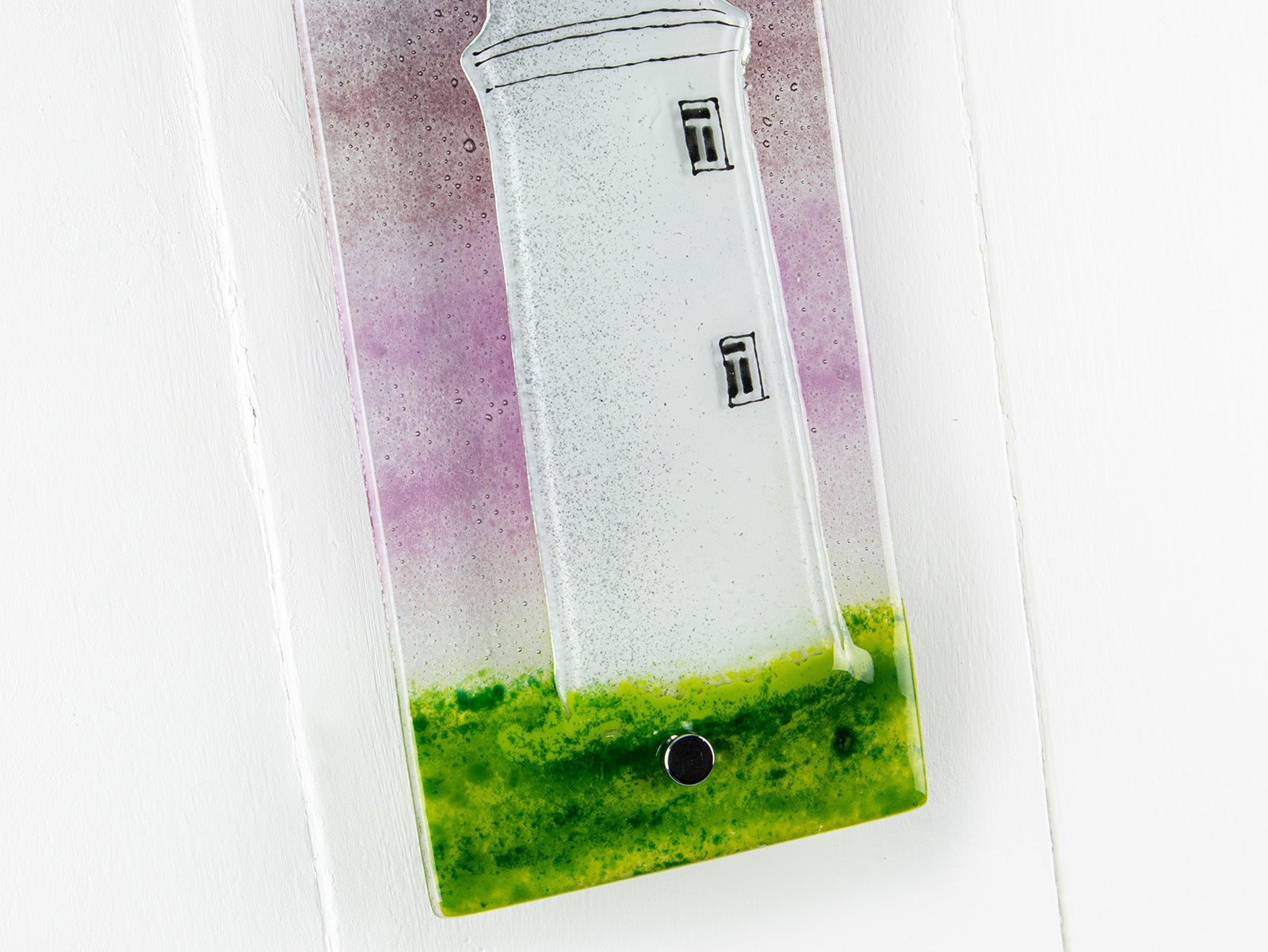 Close up of small fused glass wall panel with a Cornish lighthouse and full moon design, with coastal hues and a blushed pink sky. 