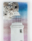 Details of small fused glass wall panel with a Cornish lighthouse and full moon design, with coastal hues and a blushed pink sky. 