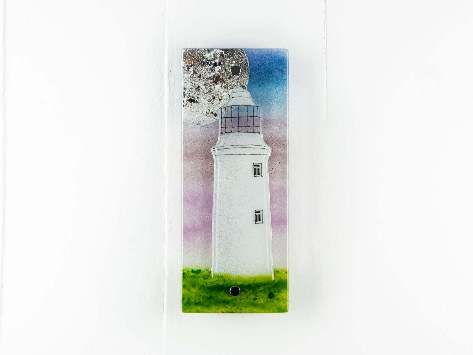 Small fused glass wall panel with a Cornish lighthouse and full moon design, with coastal hues and a blushed pink sky. 