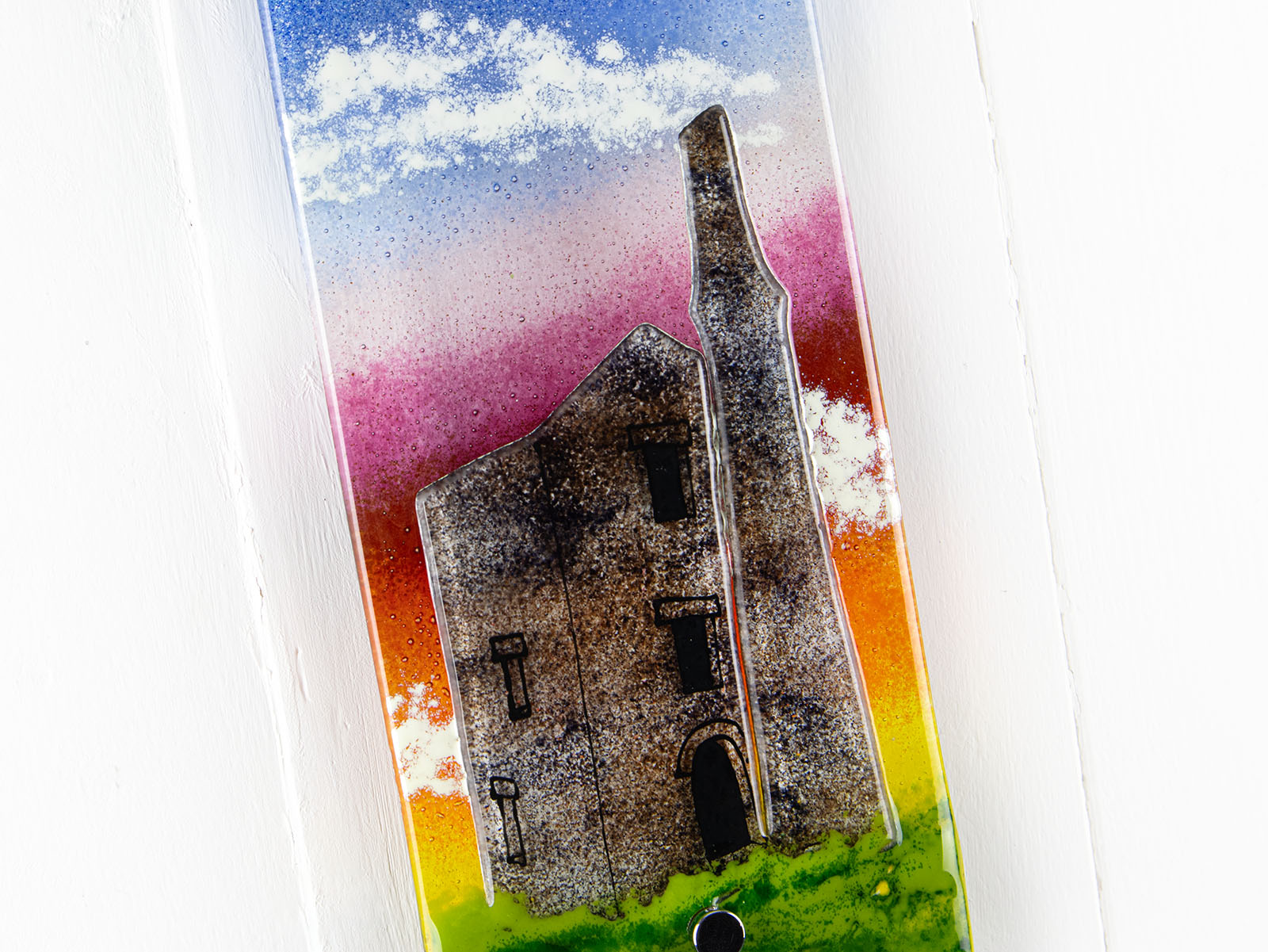 Close up of small fused glass wall panel, featuring a tin mine design, with vibrant sunset sky. 