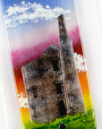 Close up of small fused glass wall panel, featuring a tin mine design, with vibrant sunset sky. 
