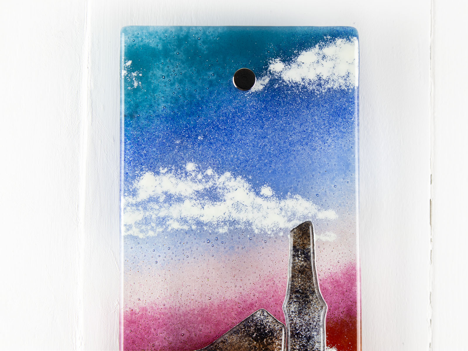 Details of small fused glass wall panel, featuring a tin mine design, with vibrant sunset sky. 