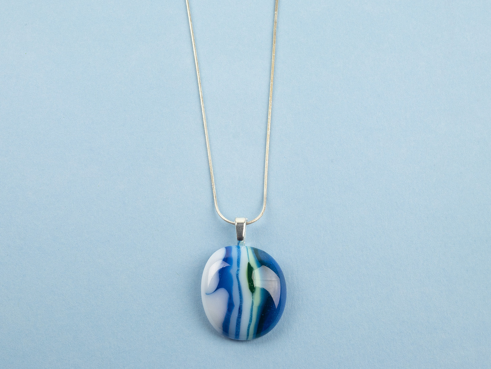 Close up of fused glass pendant necklace, handmade in coastal blues, hung on a sterling silver chain. 