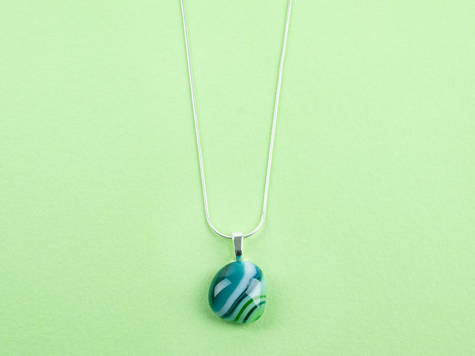 Close up of Fused glass pendant necklace, handmade with spring greens and hung on a sterling silver chain. 