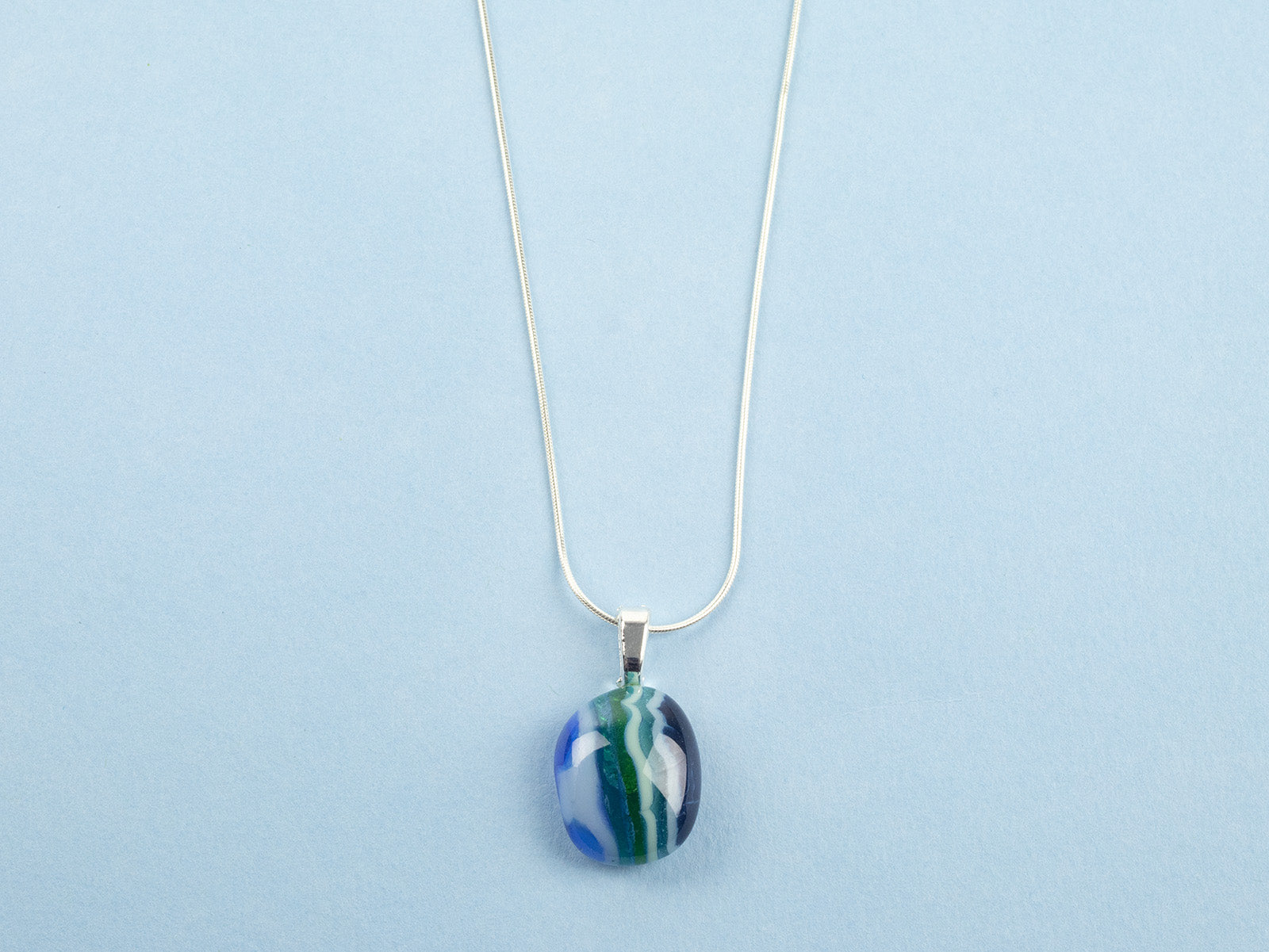 close up of fused glass necklace, handmade with ocean blues and hung on sterling silver chain.