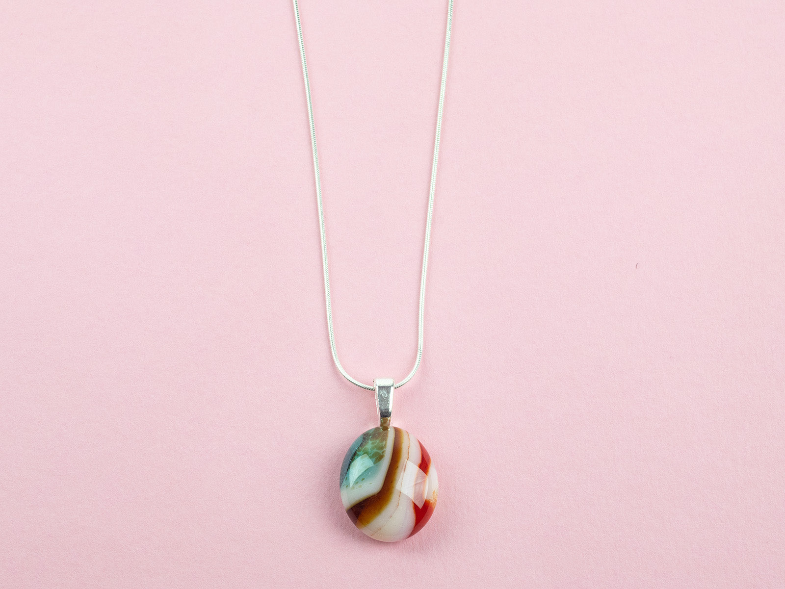 Close up of fused glass pendant necklace, handmade in sea greens and rose pinks, hung on sterling silver chain. 