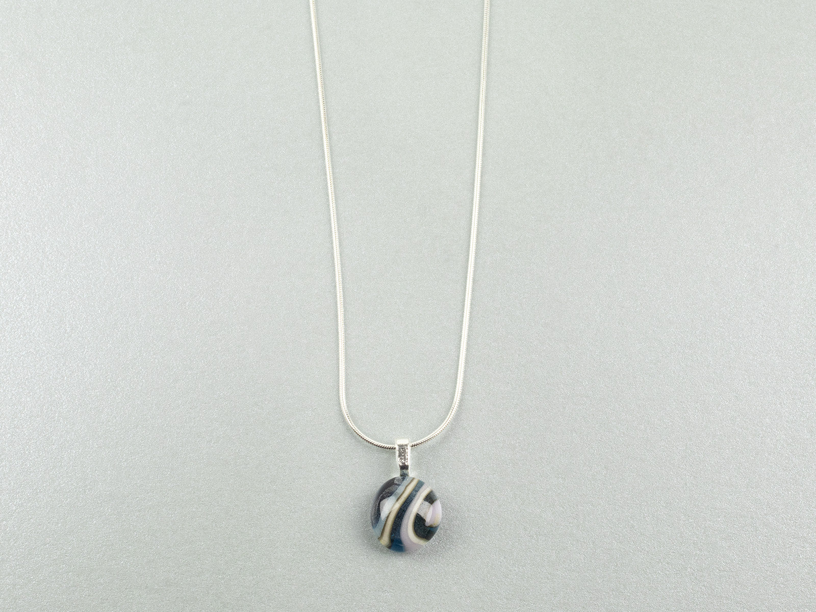 Close up of fused glass pendant necklace, handmade in soft coastal hues, hung on a sterling silver chain. 