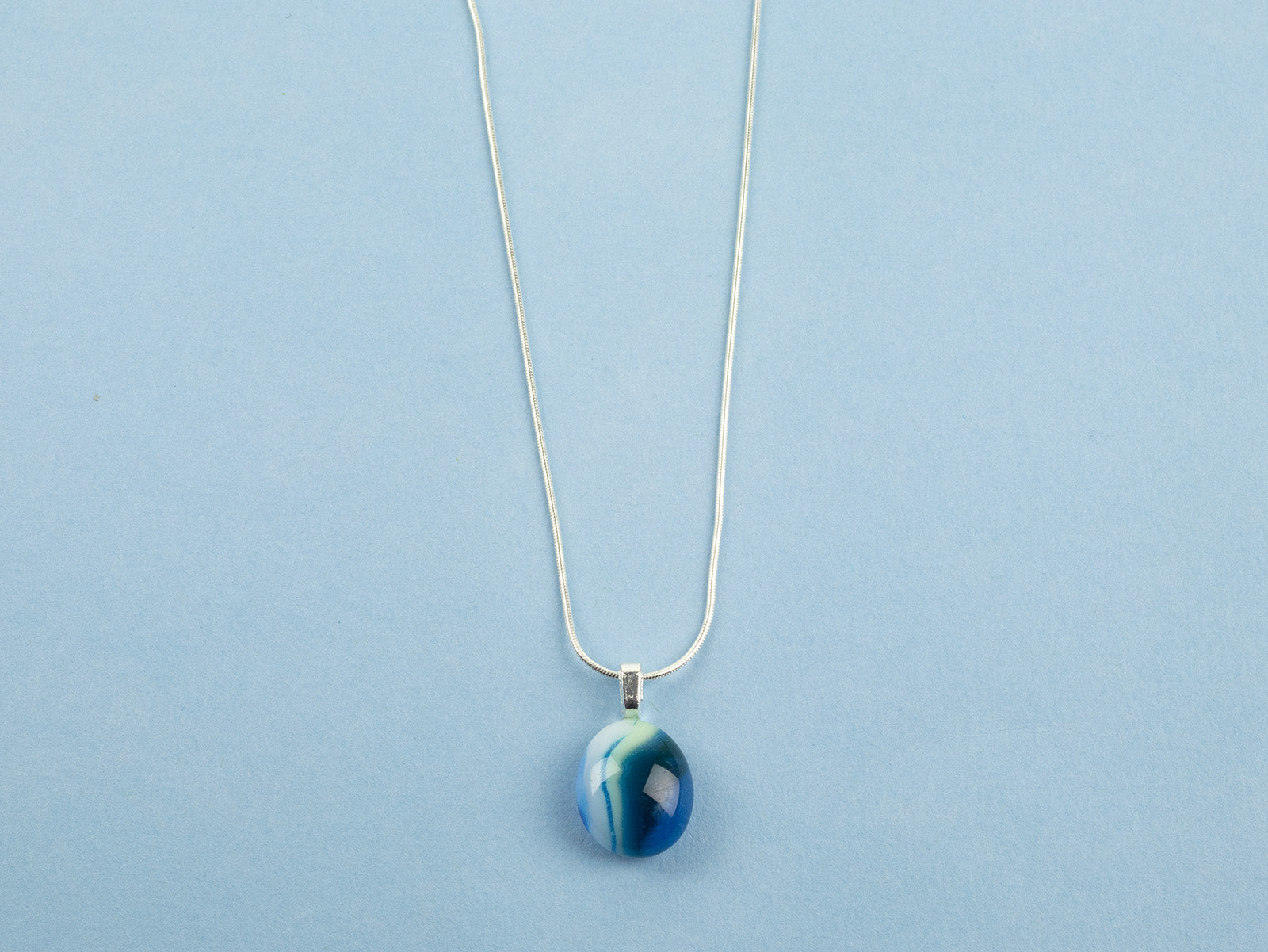 Close up of fused glass pendant necklace, handmade in marine blues, hung on sterling silver chain. 