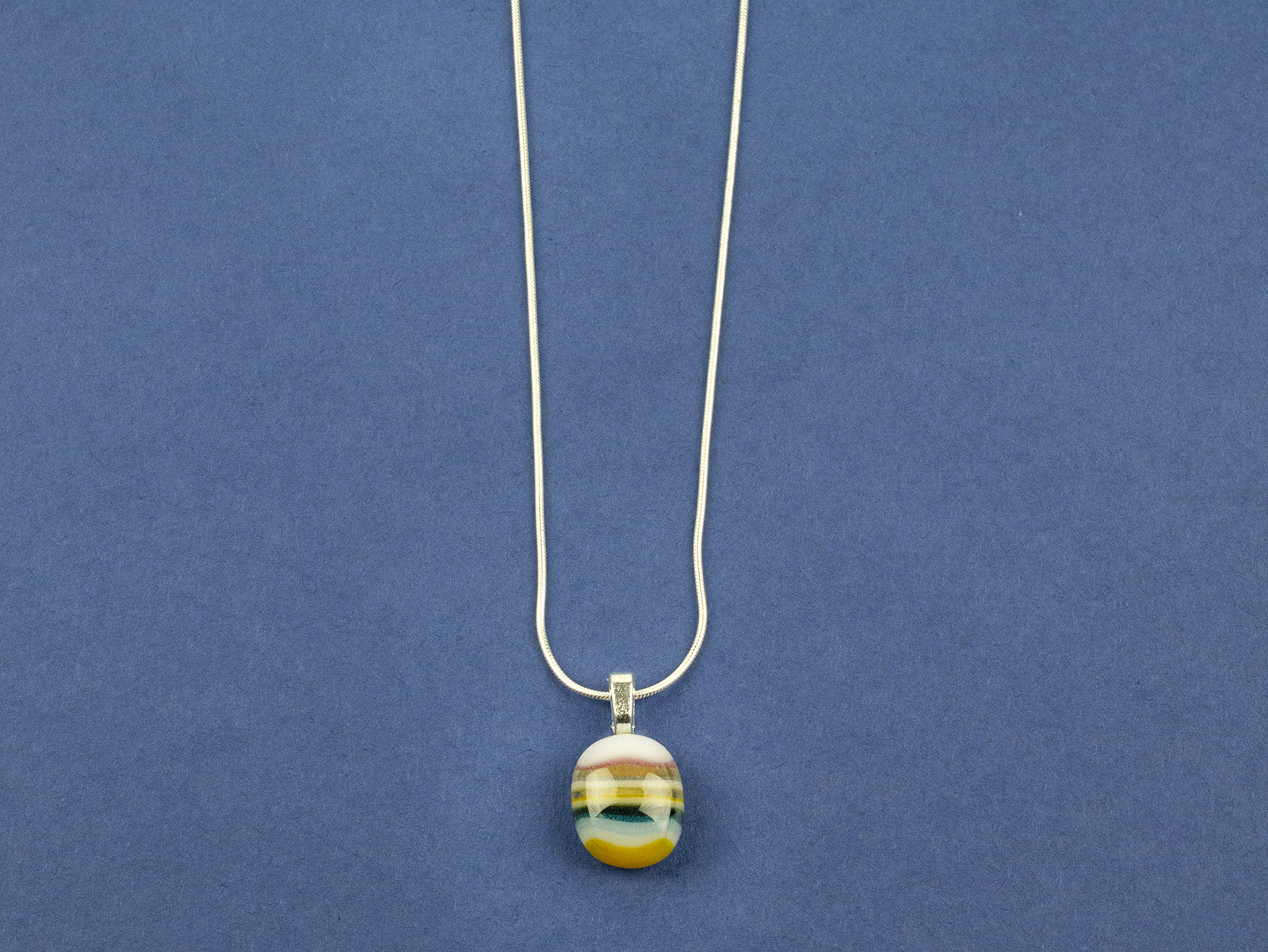 Close up of fused glass pendant necklace, handmade in soft coastal colours, hung on sterling silver chain. 