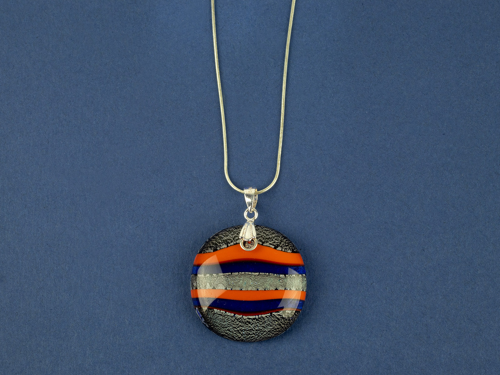 Close up of fused glass large pendant necklace in vibrant orange and purple colours. Handmade and features sterling silver chain and fixings.
