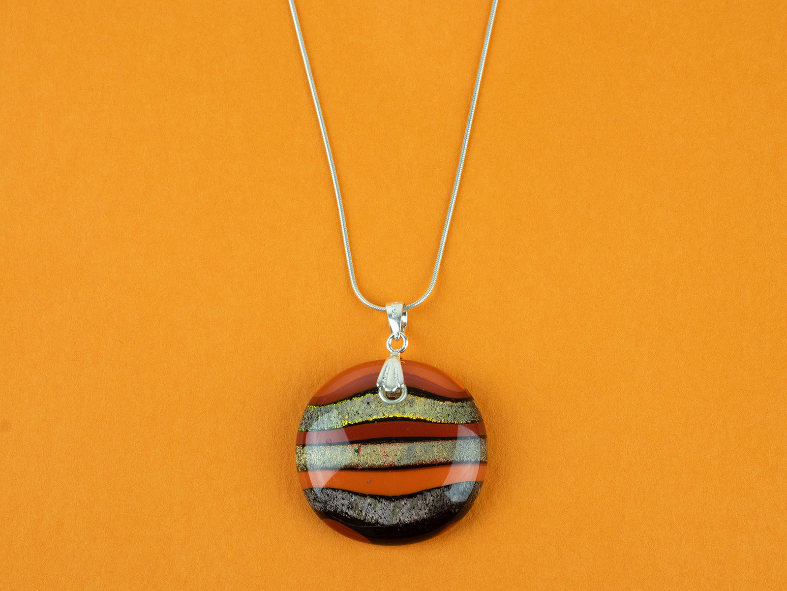 Close up of fused glass large pendant necklace in vibrant orange colours. Handmade and features sterling silver chain and fixings.