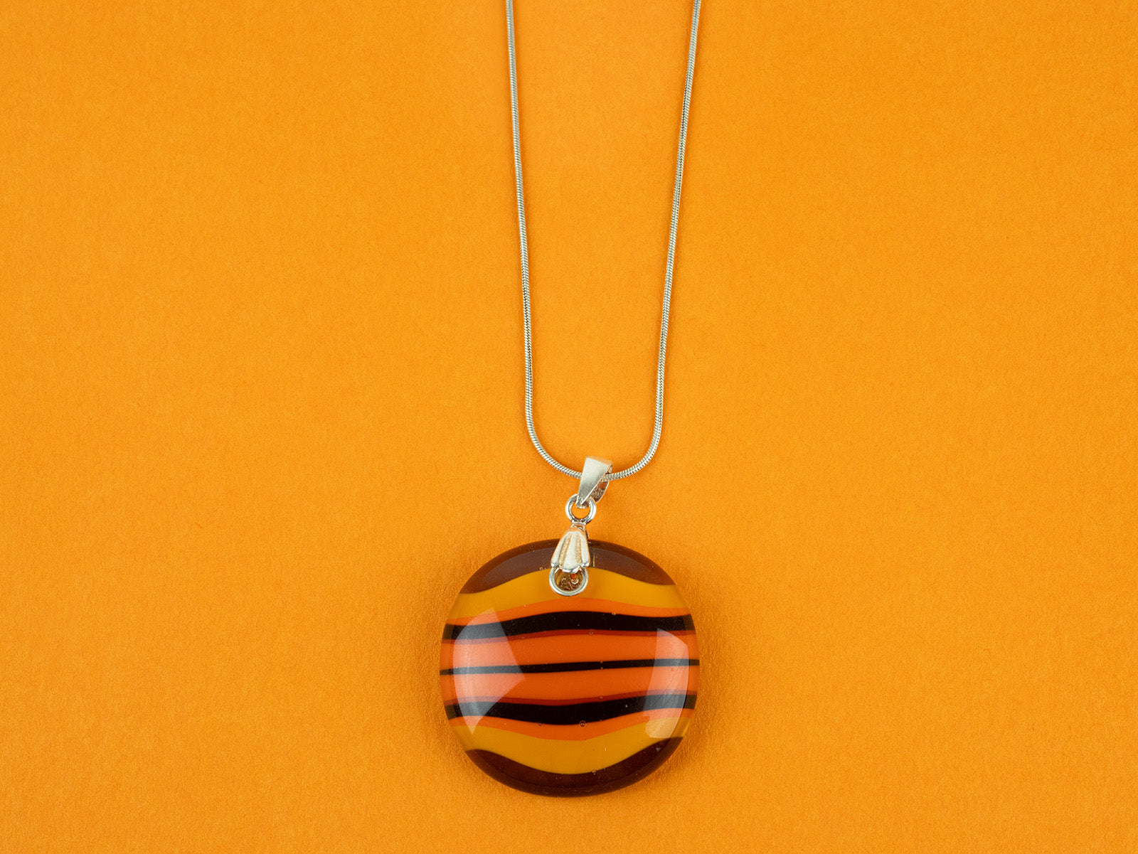 Close up of fused glass large pendant necklace in vibrant orange colours. Handmade and features sterling silver chain and fixings.