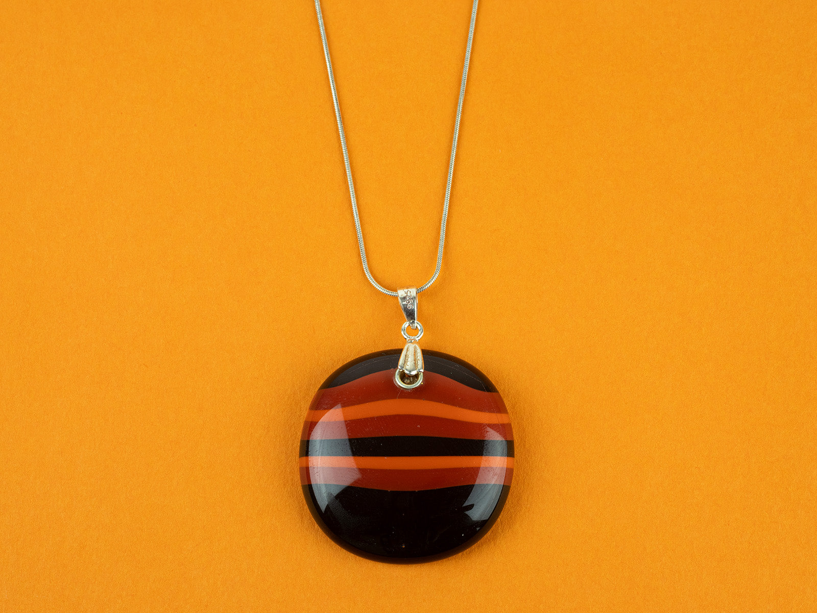 Close up of fused glass large pendant necklace in vibrant orange colours. Handmade and features sterling silver chain and fixings.