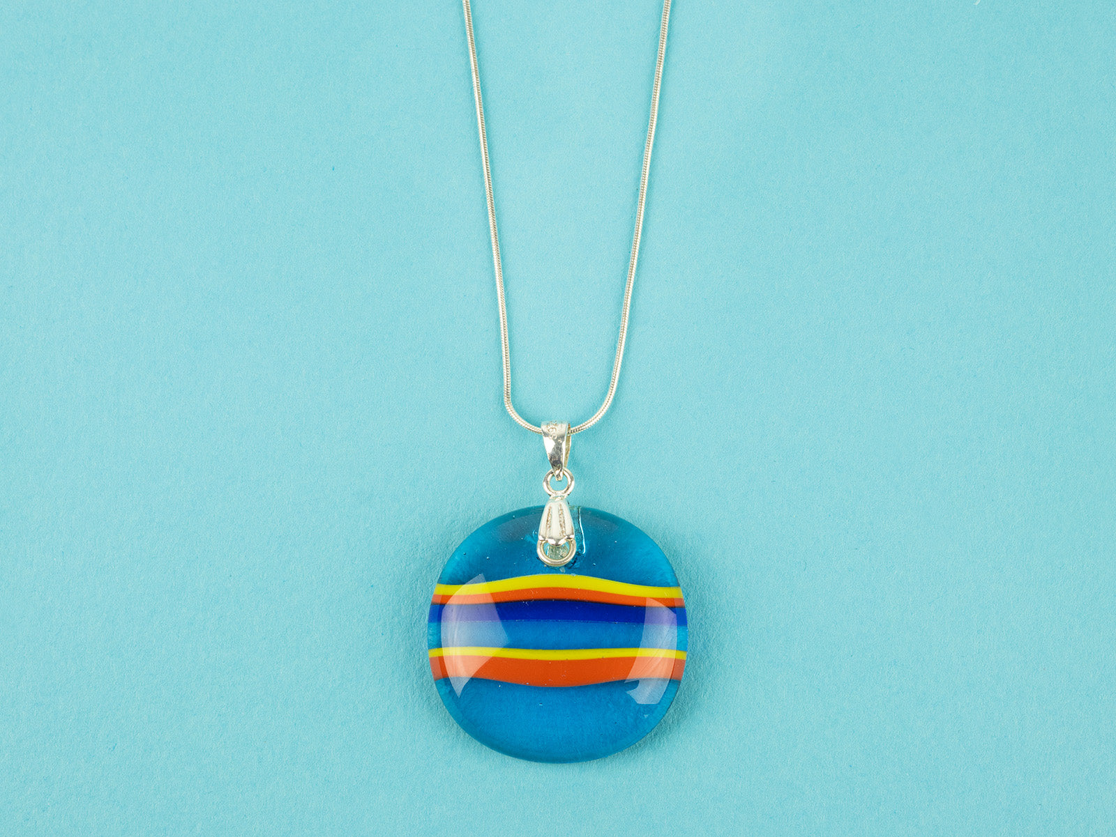 Close up of fused glass large pendant necklace in vibrant orange and aqua blue colours. Handmade and features sterling silver chain and fixings.
