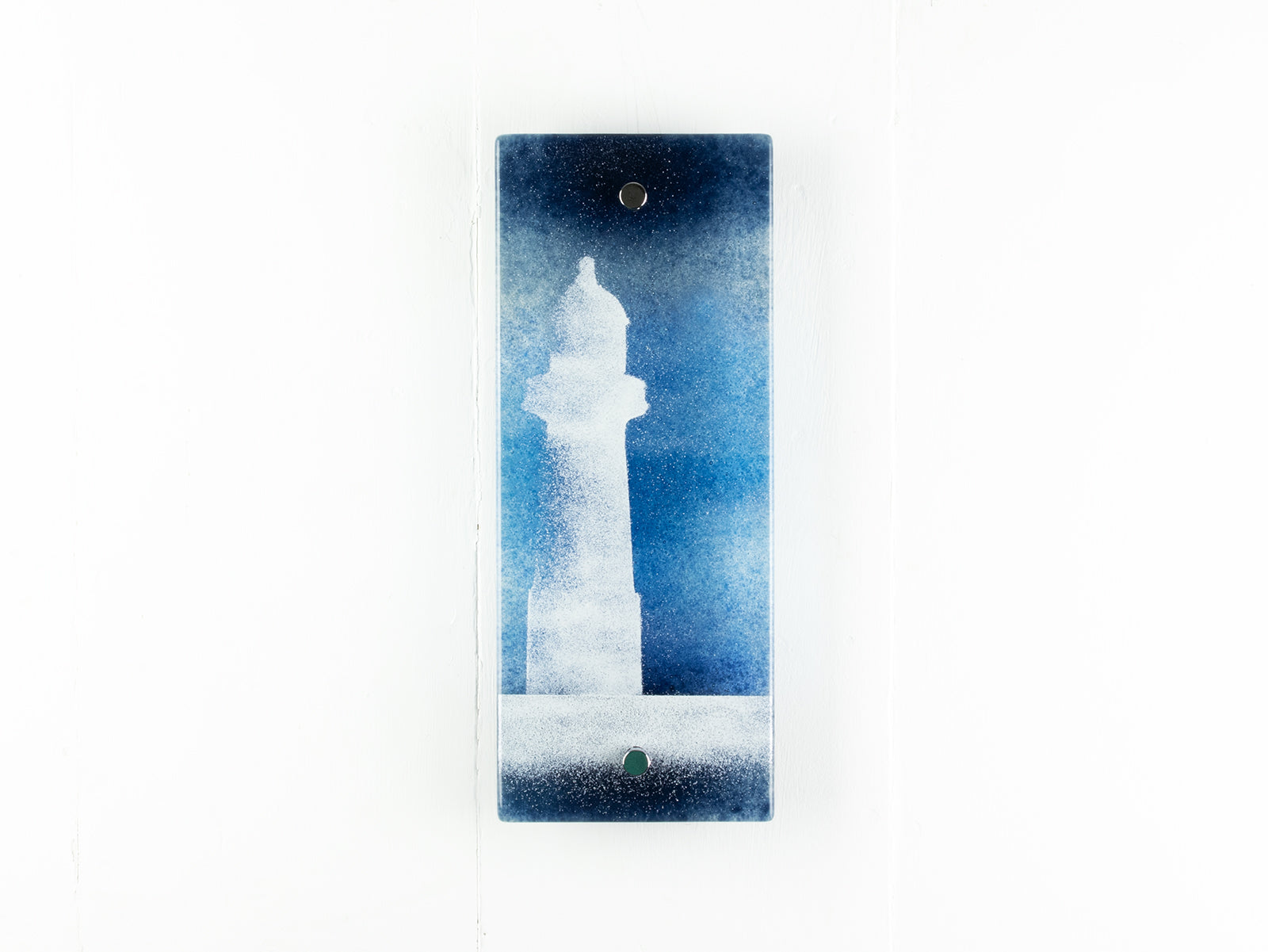 Fused glass wall pane with a mystical design of a lighthouse against a teal blue background. 