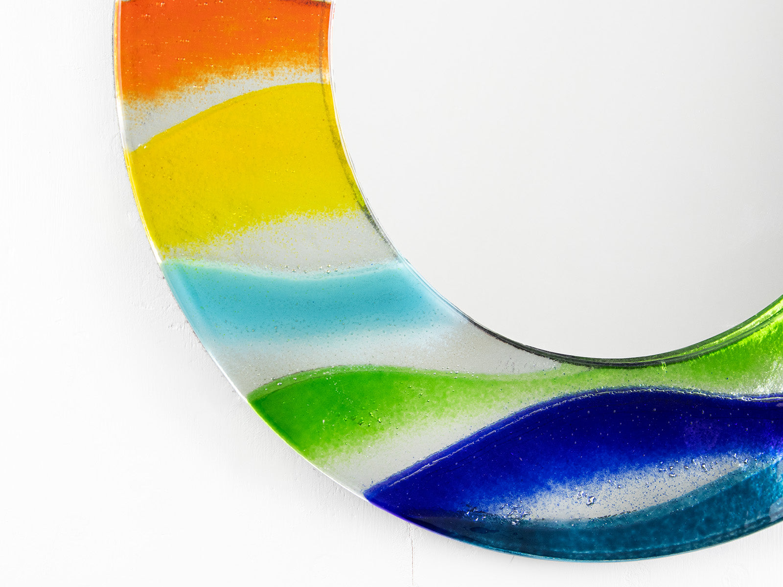 Close up of colourful fused glass mirror, handmade with rainbow colours.