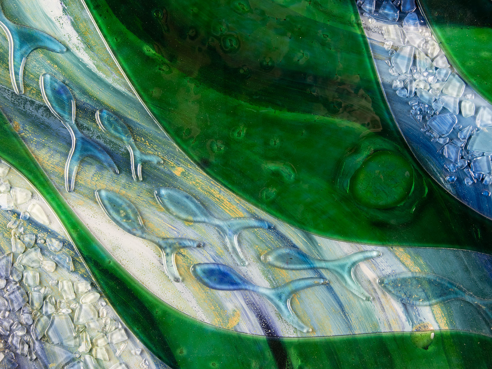 Close up of glass fish on a fused glass oblong art frame with coastal greens and textural blues.