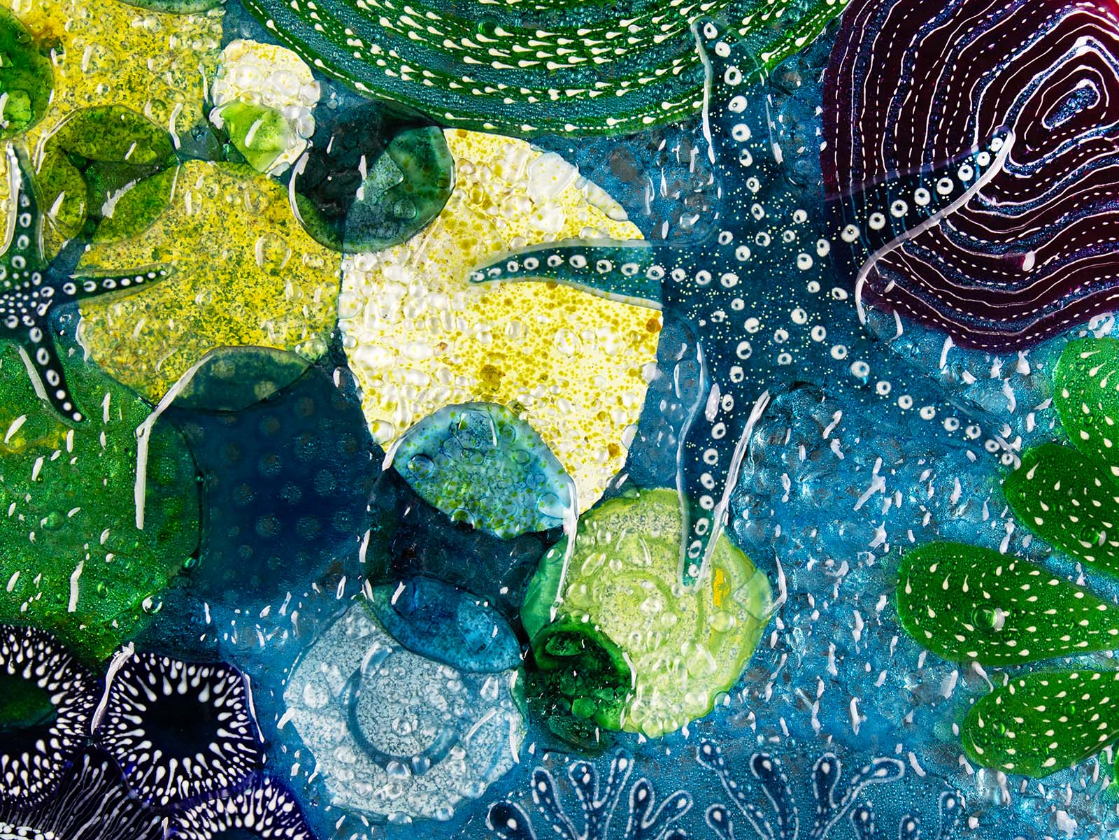 Close up of round wall panel made from fused glass, inspired by the ocean reefs with starfish detailing and coastal colours. 
