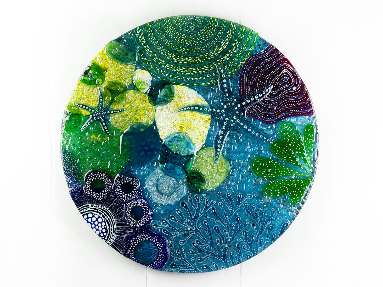 Round wall panel made from fused glass, inspired by the ocean reefs with starfish detailing and coastal colours. 