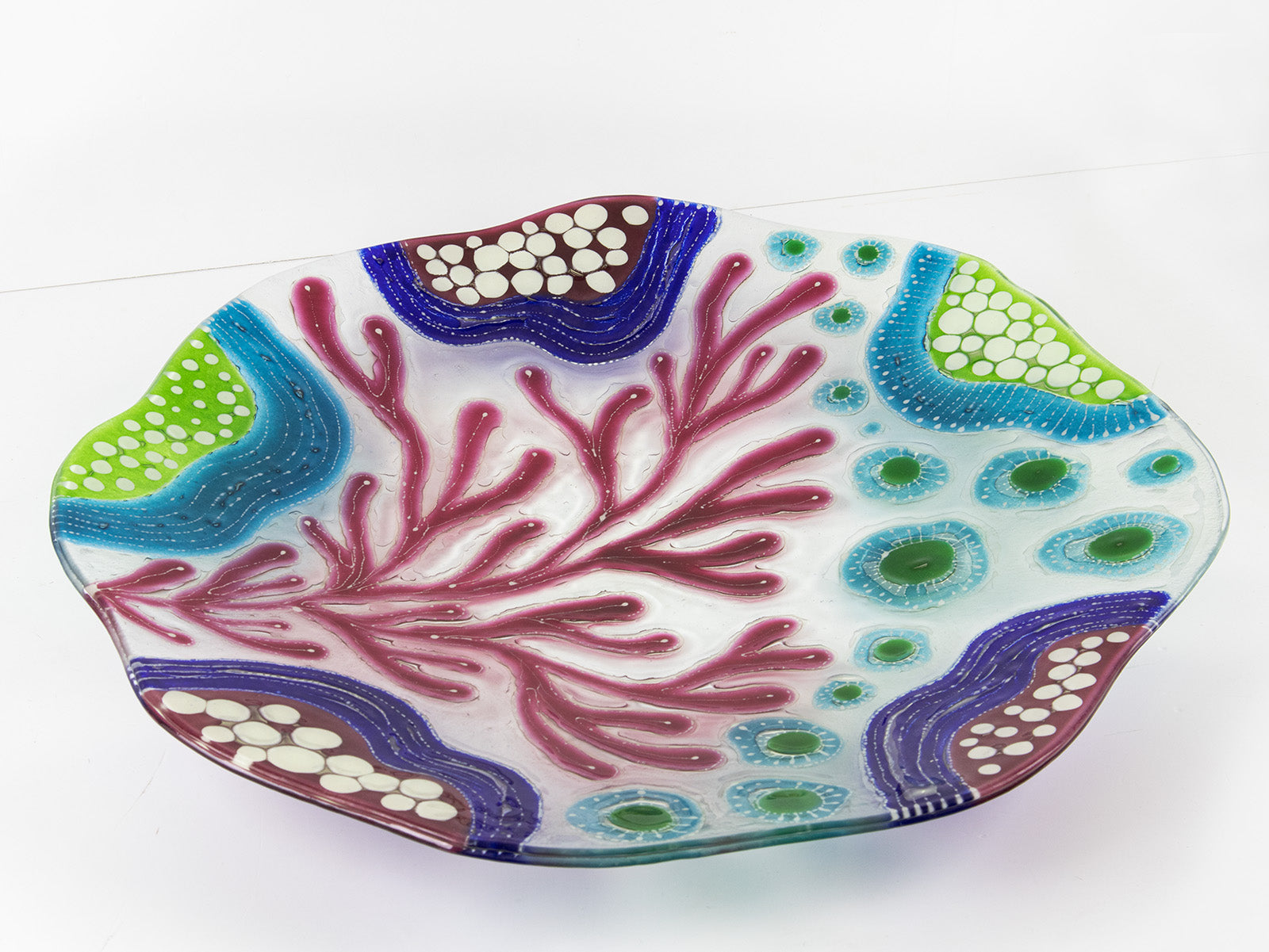 Table image of fused glass round dish, with hand painted design inspired by the ocean reefs in bright colours. 