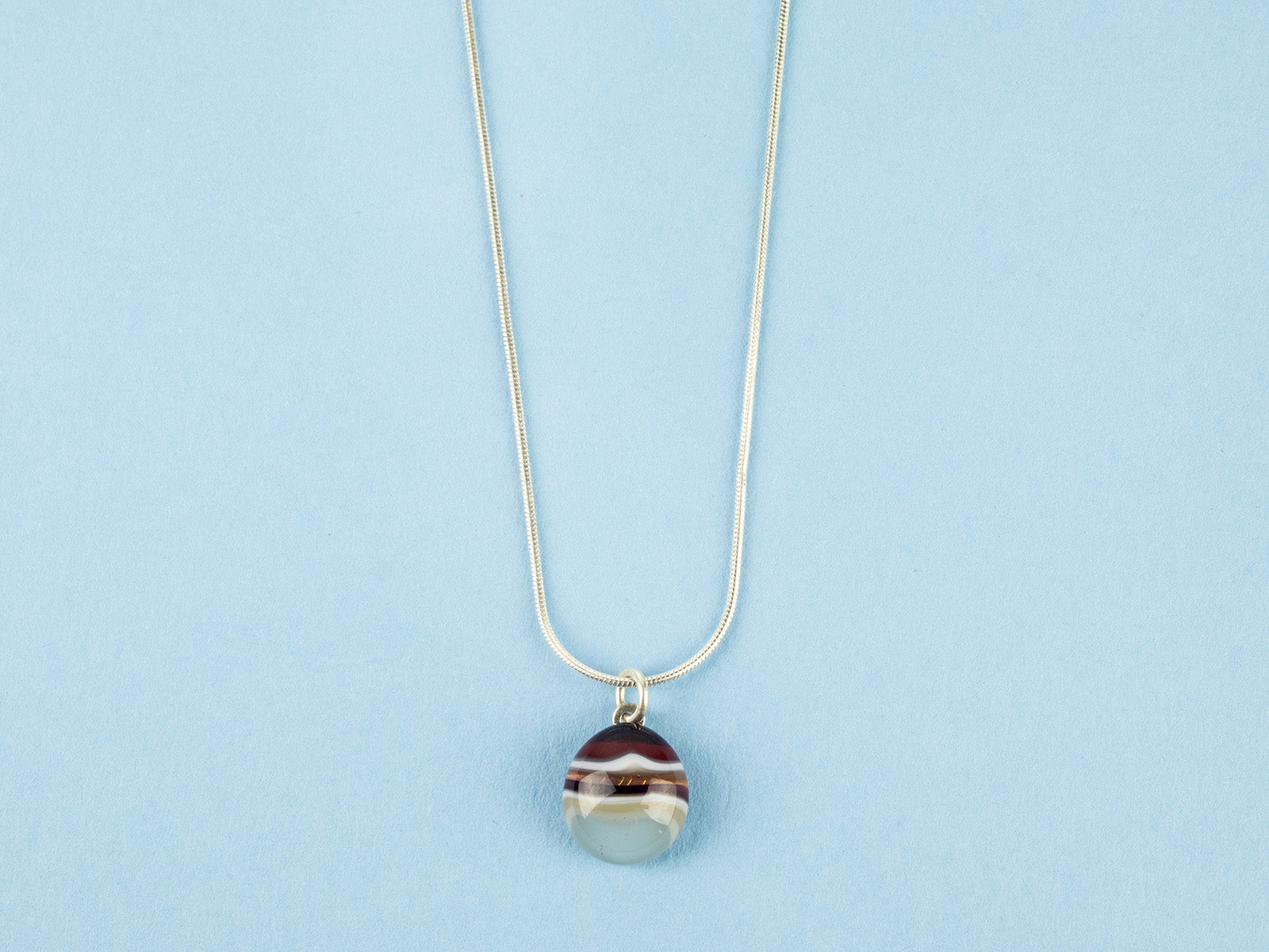Close up of fused glass pendant necklace, handmade with ruby red and marine blue colours. Stunning jewellery with sterling silver chain. 