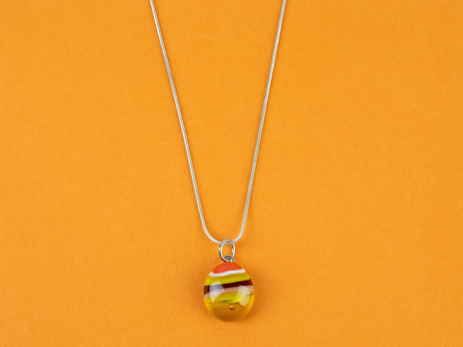 Close up of fused glass pendant necklace, handmade with sunset orange and yellow colours. Stunning jewellery with sterling silver chain. 