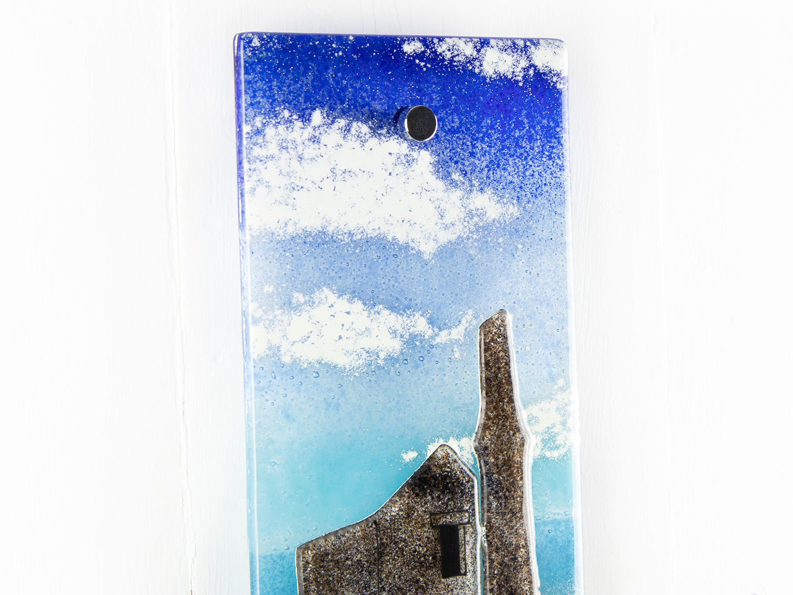 Close up of a fused glass wall panel with details featuring fluffy white clouds  on a tin mine design. 