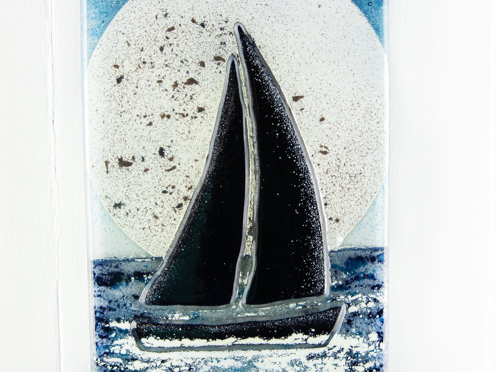 Close up of sail boat with full moon behind, hand-made onto a fused glass small wall panel with deep teal colour-way and texture.