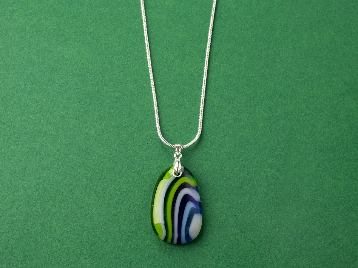 An artisan fused glass pendant necklace in coastal blues and greens, handcrafted in our studio. Finished with a sterling silver chain and fittings, a striking piece of wearable art.