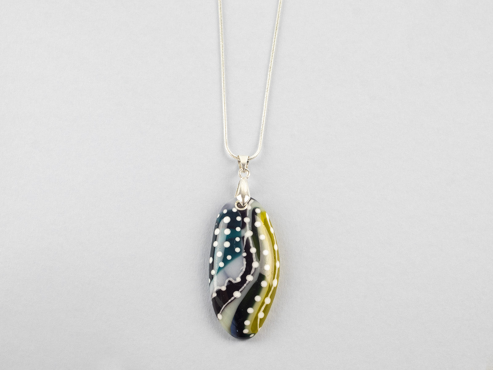 A fused glass pendant necklace on a sterling silver chain, handmade with soft coastal colours, with hand-painted dots and swirls. 