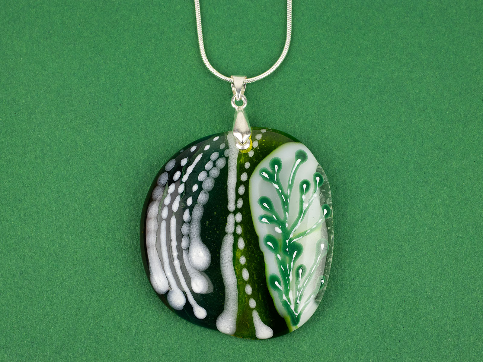 Close up of fused glass pendant necklace, handmade in spring greens, with botanical hand-painted design. 