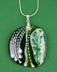 Close up of fused glass pendant necklace, handmade in spring greens, with botanical hand-painted design. 