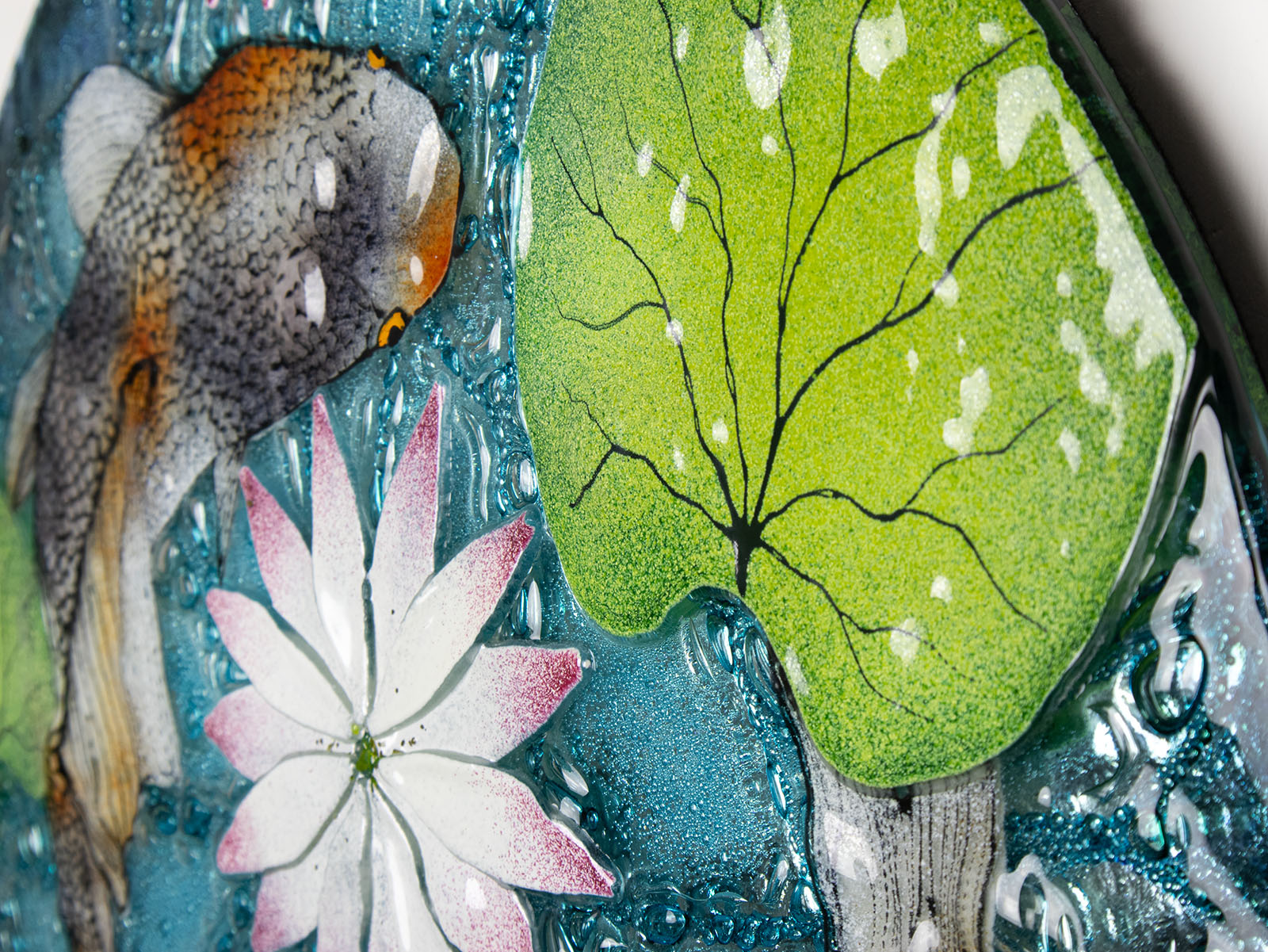 A close up of the leaf in a fused glass round panel featuring hand-painted koi carp design with waterlilies and marine blue background. 