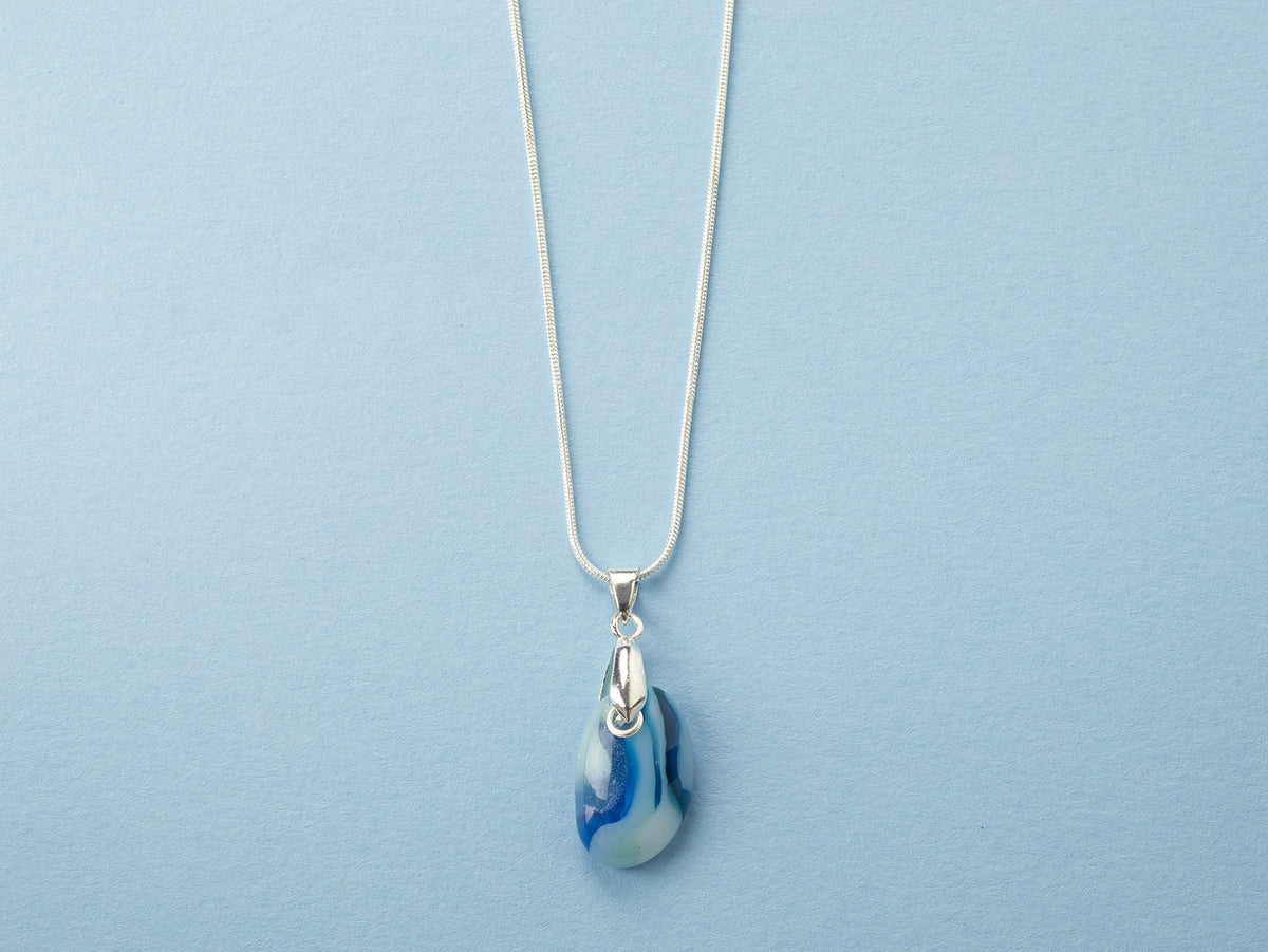 A sterling silver chain necklace with a teardrop-shaped fused glass pendant handmade featuring a ocean blue marbled design. 