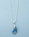 A sterling silver chain necklace with a teardrop-shaped fused glass pendant handmade featuring a ocean blue marbled design. 