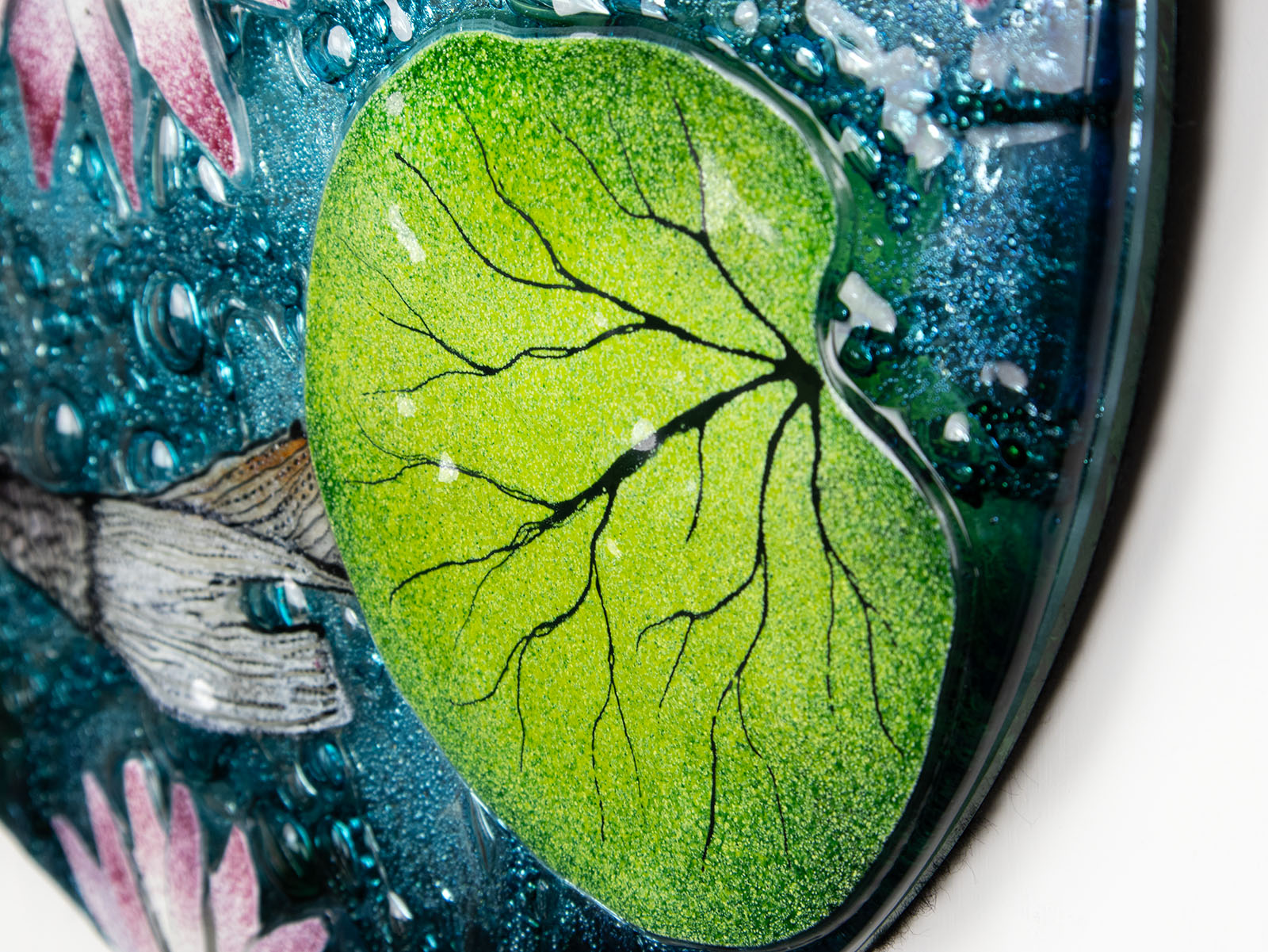 Leaf details on a fused glass round panel featuring hand-painted koi carp design with waterlilies and marine blue background. 