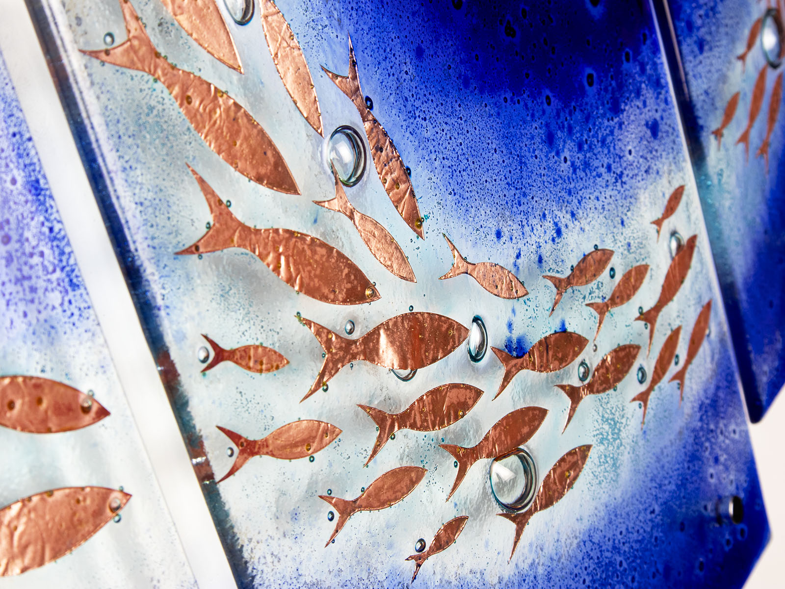 Close up of a fused glass triptych featuring a royal blue colour-way, with swirling copper fish, handmade in a beautiful ocean inspired design. 