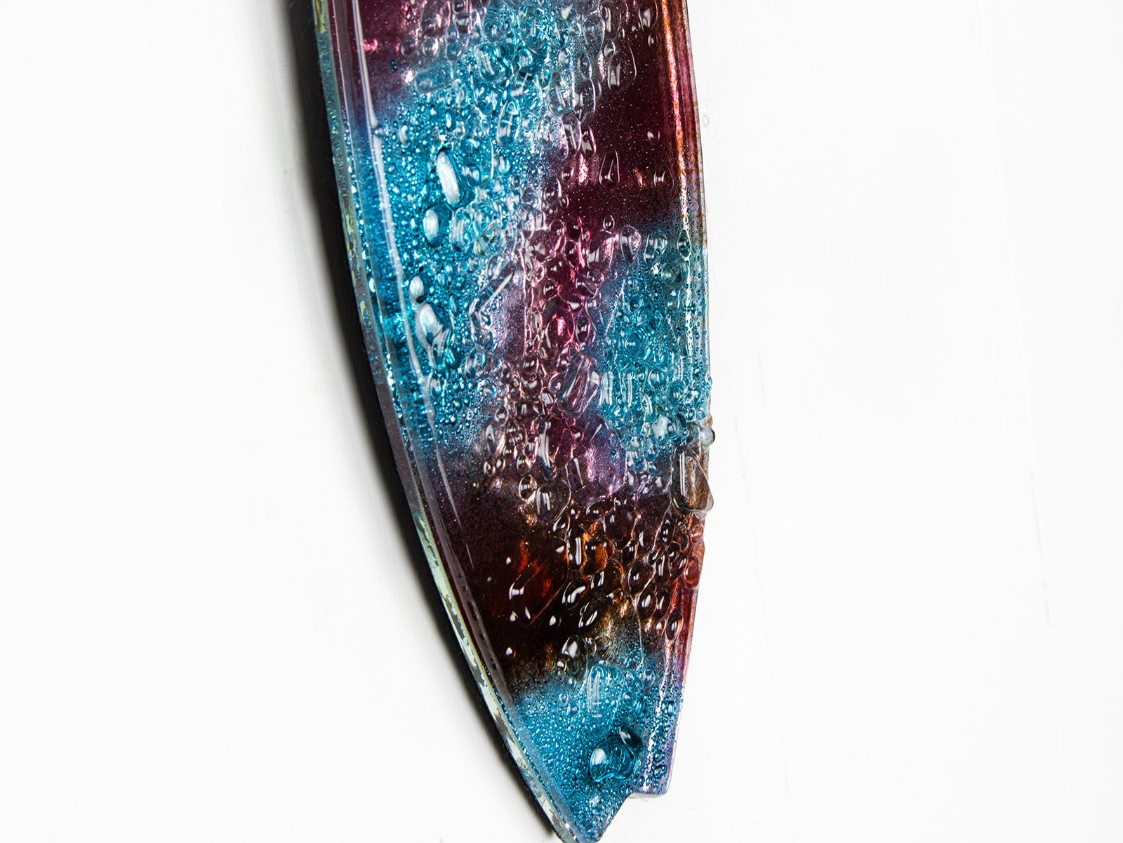 A close up of fused glass surfboard wall panel, handmade in coral pink hues and ocean blues, with textural detailing. A coastal inspired piece of wall art.  