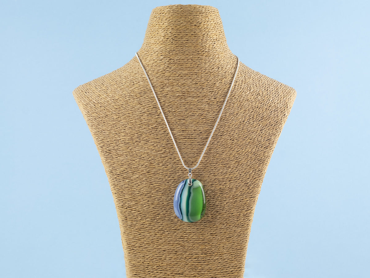 An artisan fused glass pendant necklace, handcrafted in our studio in soft coastal colours. Finished with a sterling silver chain and fittings, shown on a mannequin. 