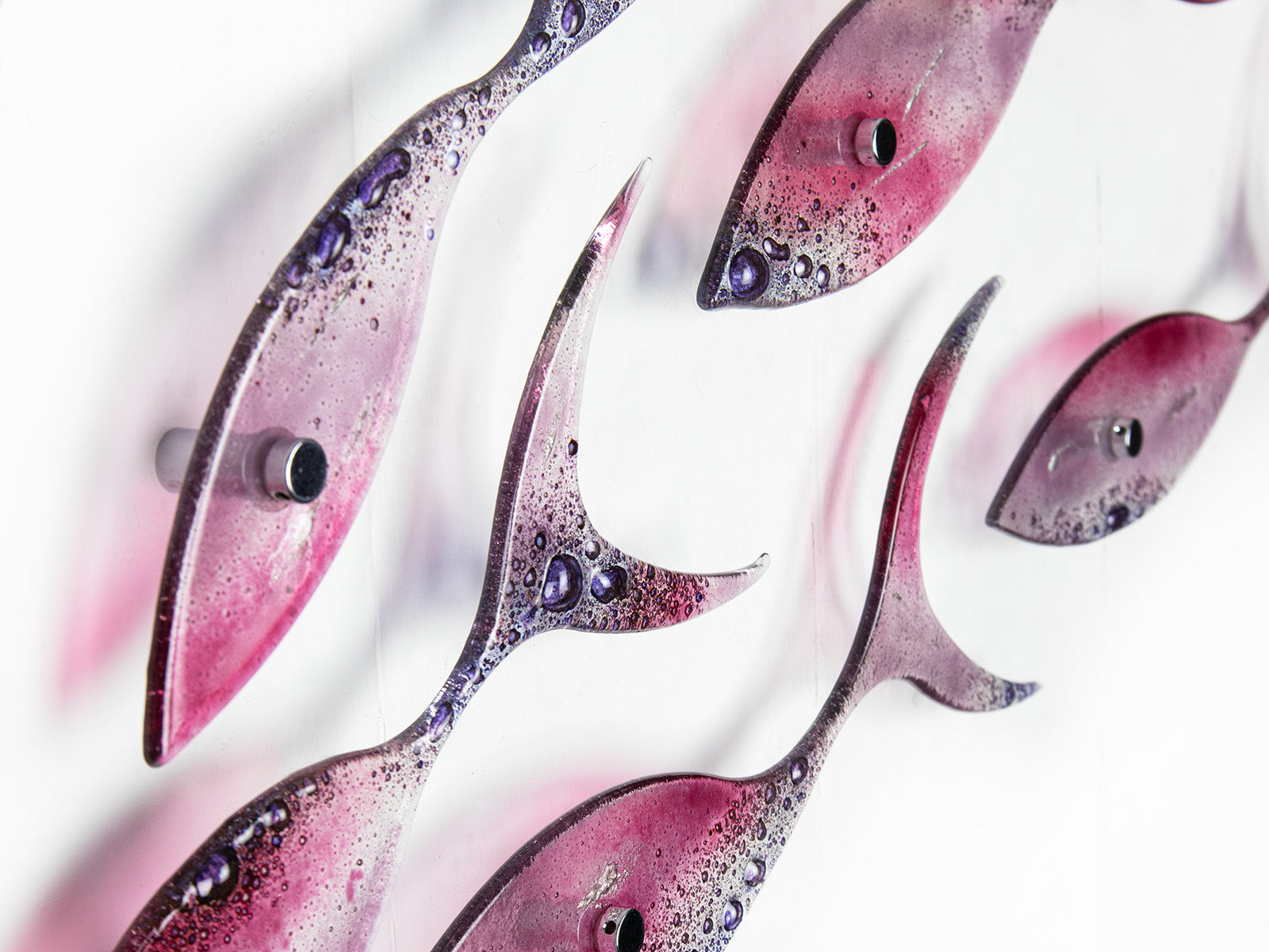 A close up of a fused glass shoal of fish, with individual fish installed in a bright pink and bubbled purple colour-way. 