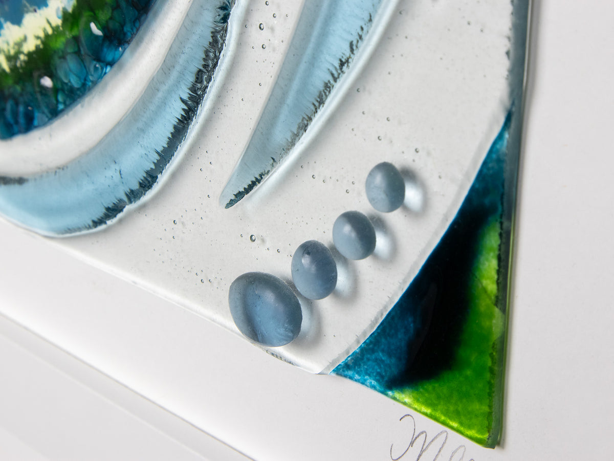 A detailed of a a fused glass large oblong art frame featuring an abstract tidal design in ocean blue and greens with textural detailing. A handmade coastal inspired piece of wall art. 
