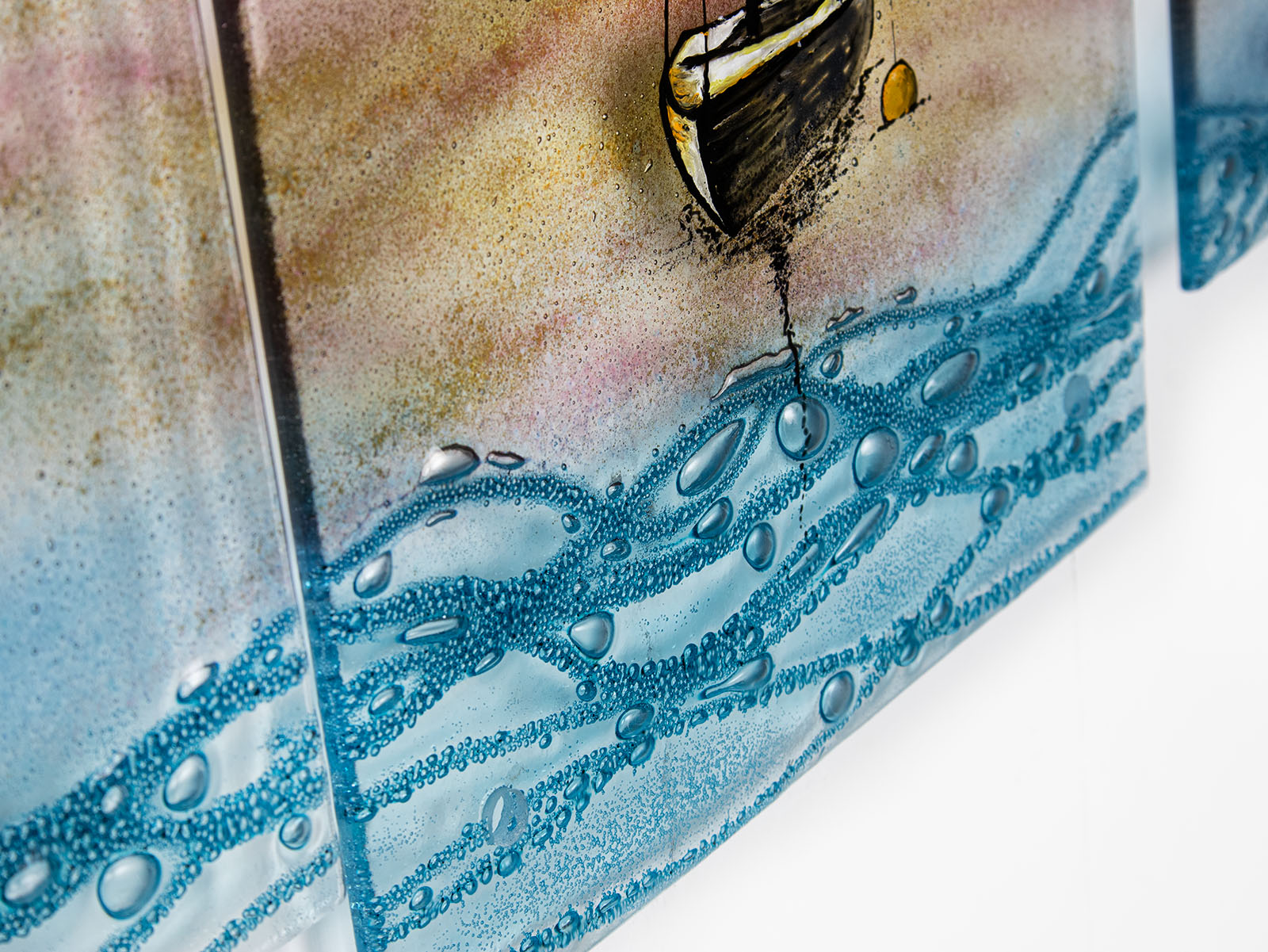 Textured detailed on a fused glass triptych depicting a serene harbour scene with hand-painted sailboats on blue water under a pastel sky with hills in the distance.