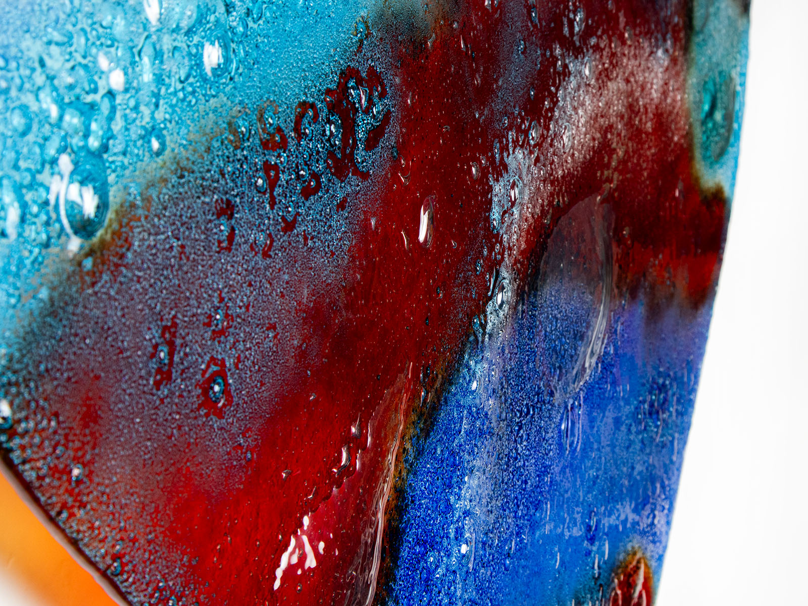 Bubbled close up shot of a striking 95cm fused glass hear shaped wall panel handcrafted in Cornish studio in bright reds, aqua blues and lots of textured detailing. 